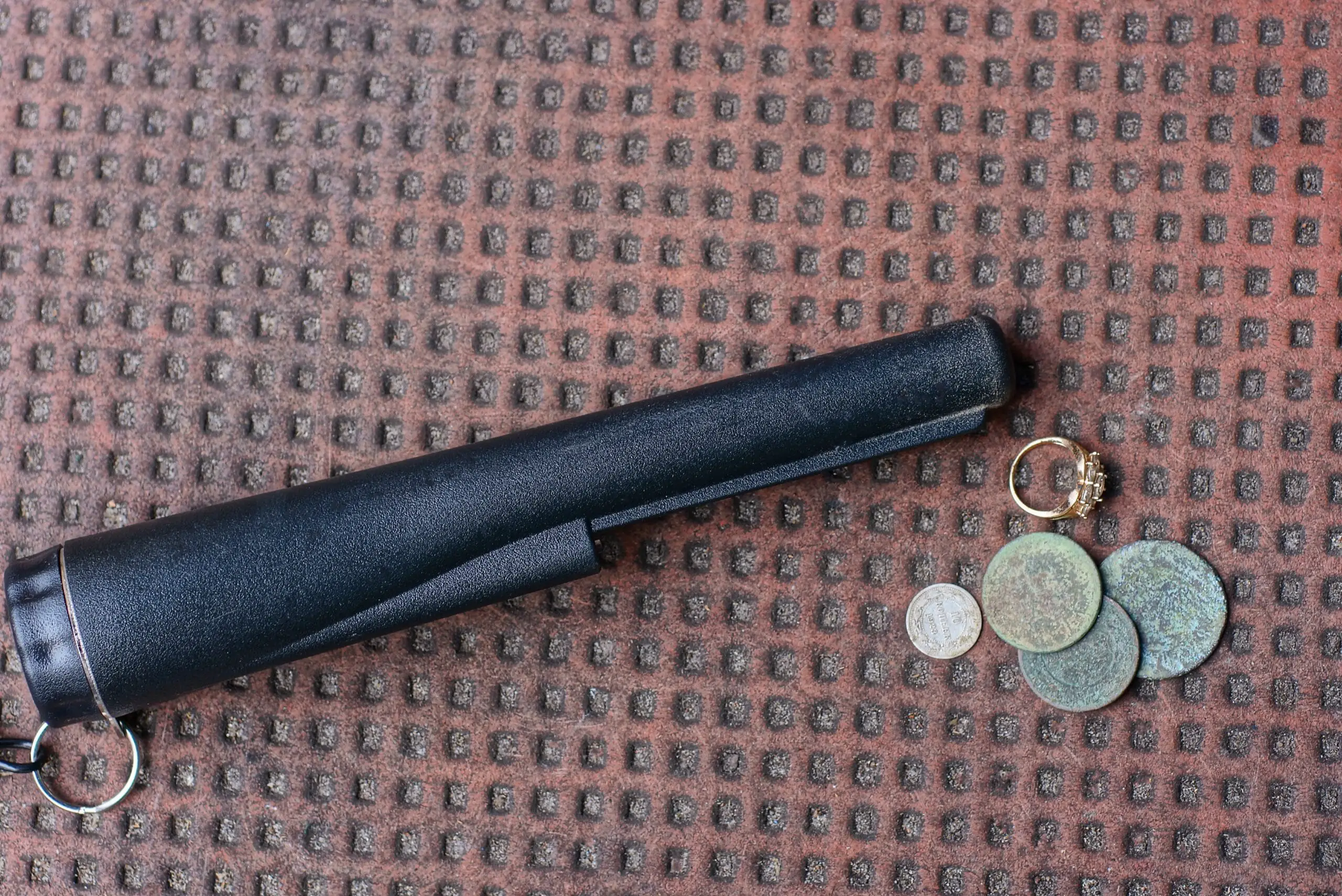 one black pinpointer lies on a brown table next to old coins