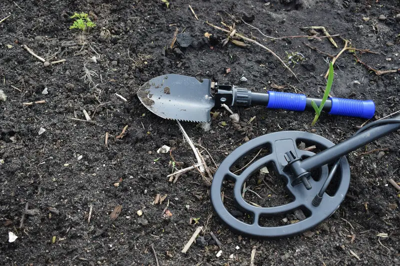 Small spade and metal detector on dark dirt