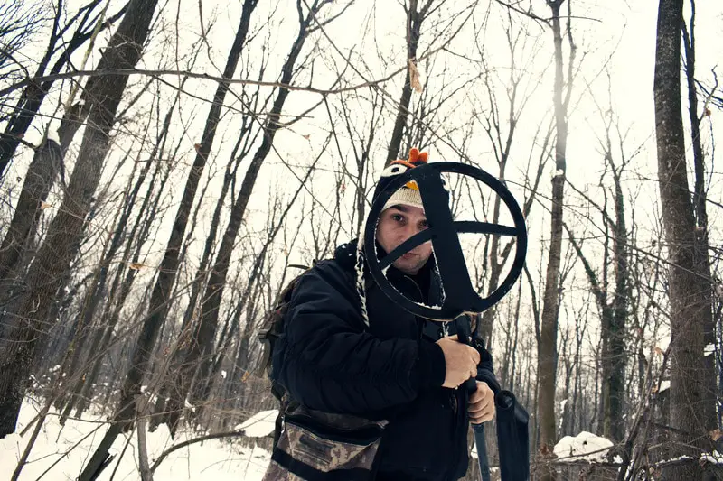 Person holding a large size search coil in the woods.