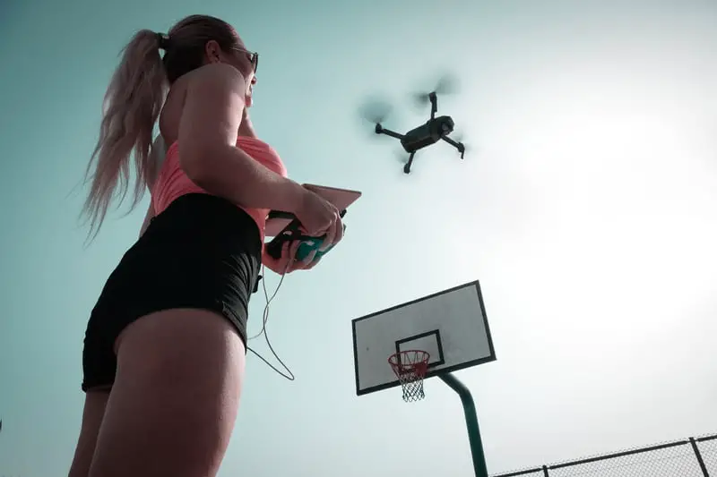 Woman Standing Near Basketball Hoop Controlling Drone