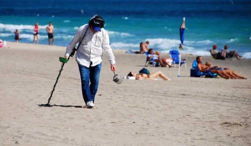 Man searching the beach with a metal detector and sand scoop.