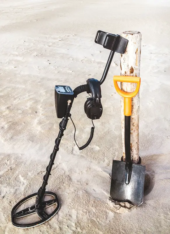 Metal detector and shovel leaning against a post on the beach.