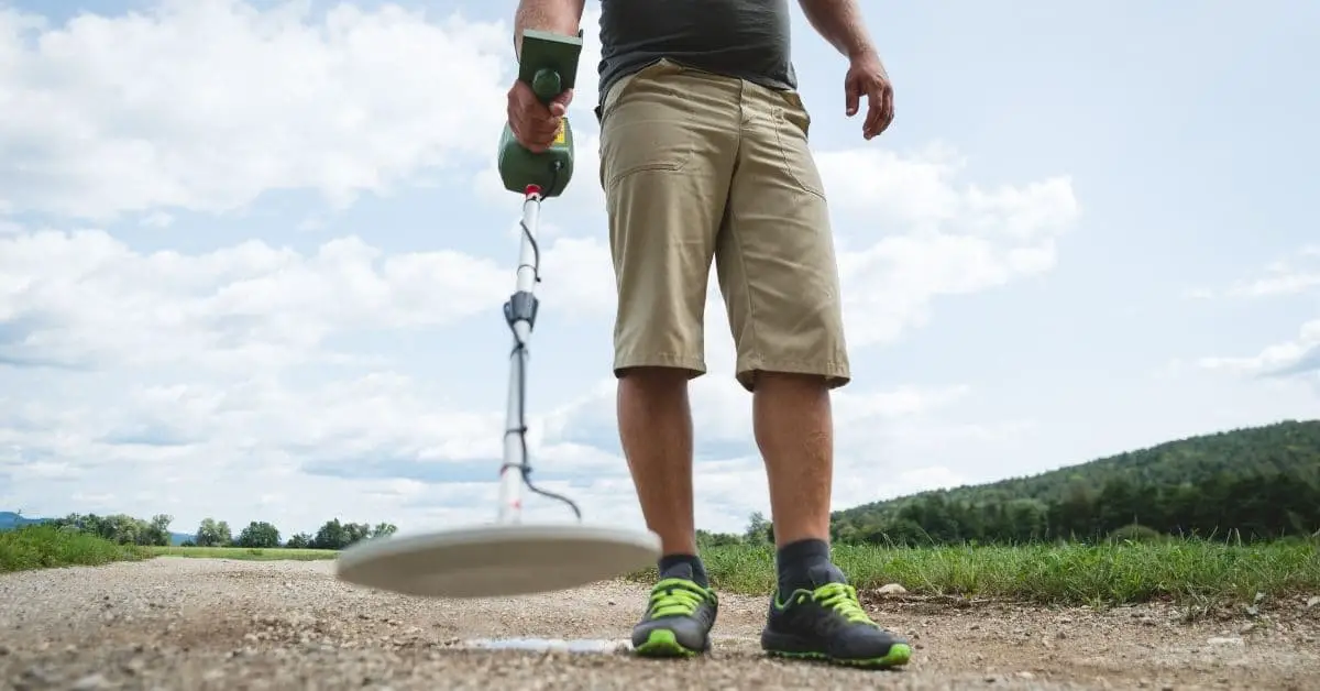 Man metal detecting on a dirt road.