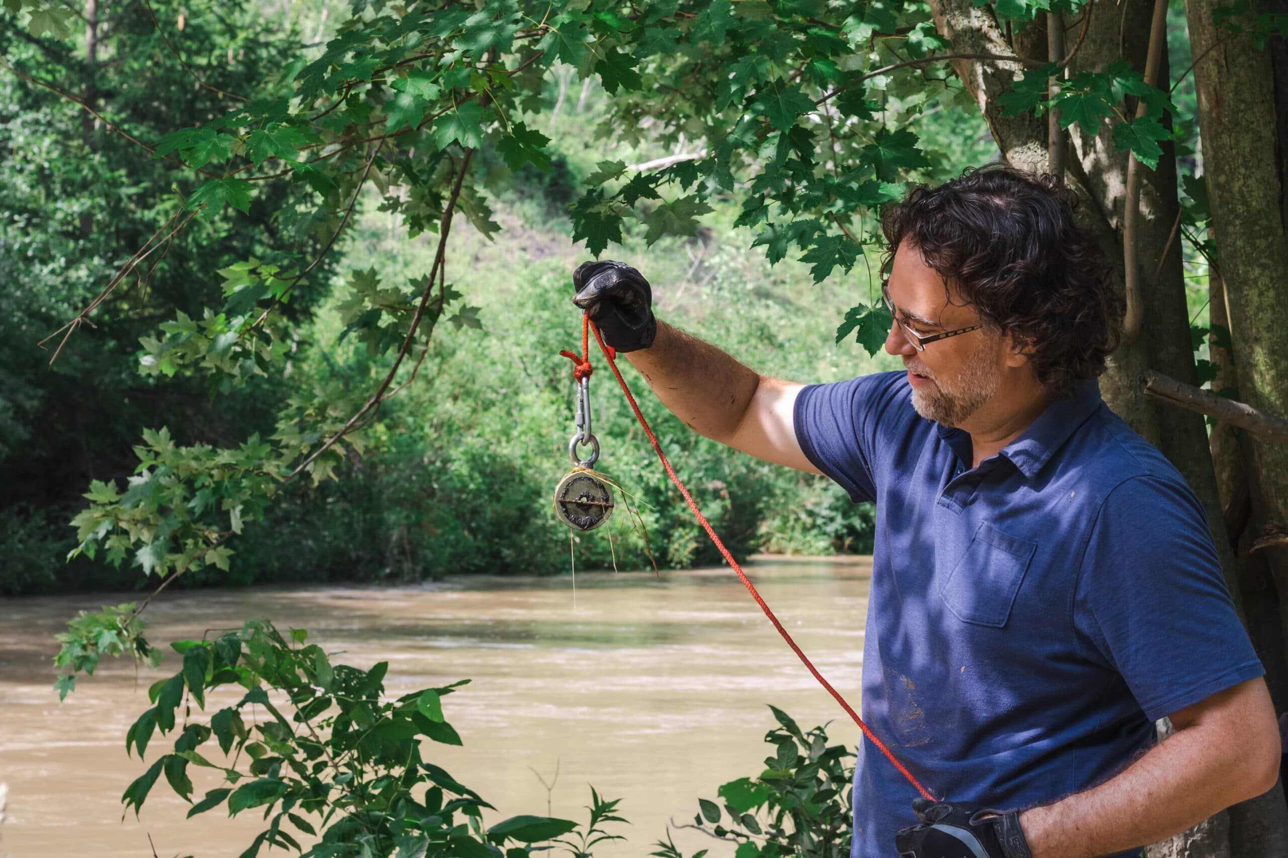 man looking at metal he's found while magnet fishing on a river.