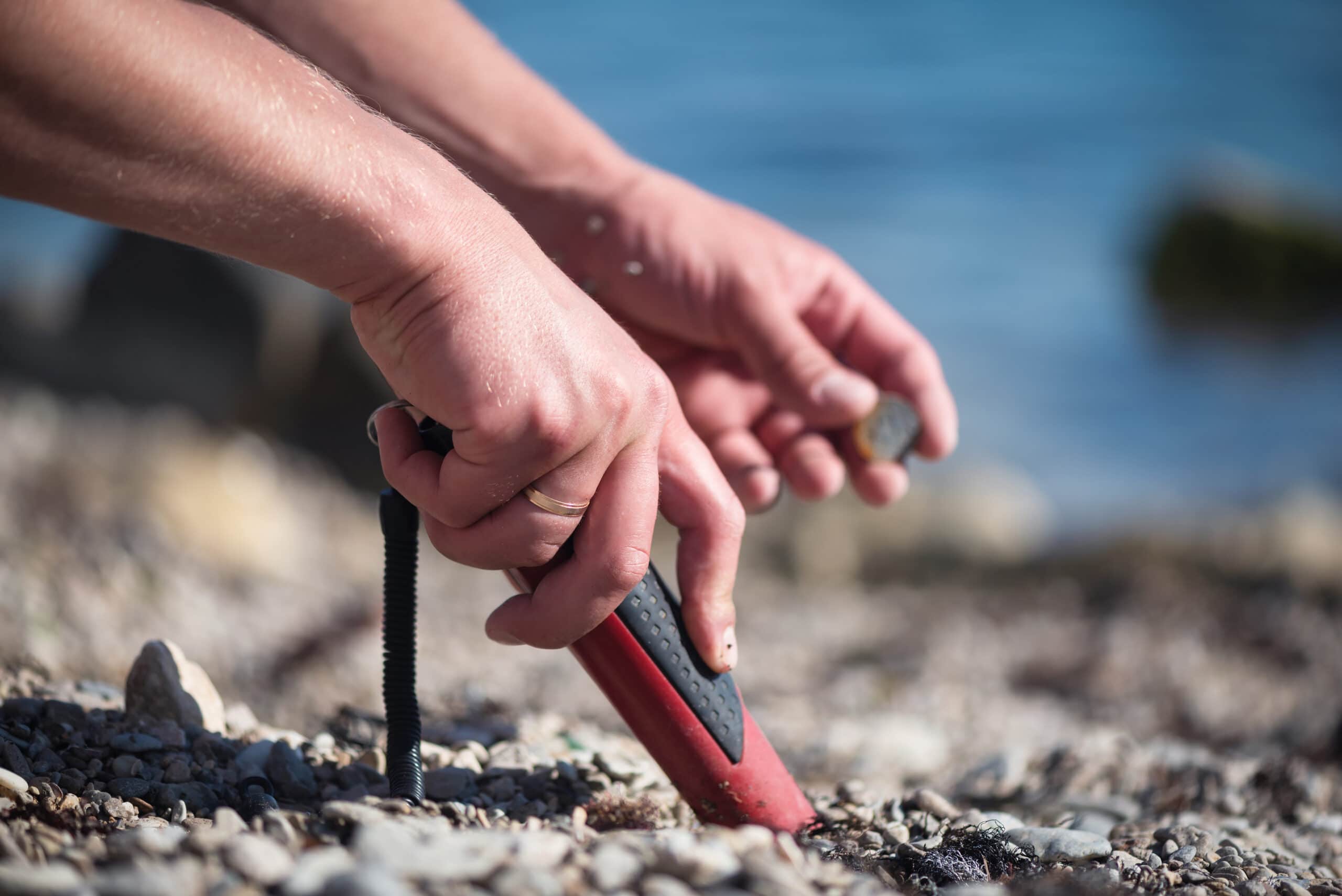 Man with a pin pointer metal detector on the sea beach is looking for the lost coins.